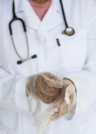Image of a doctor in a white coat with a stethoscope around their neck putting on medical gloves.